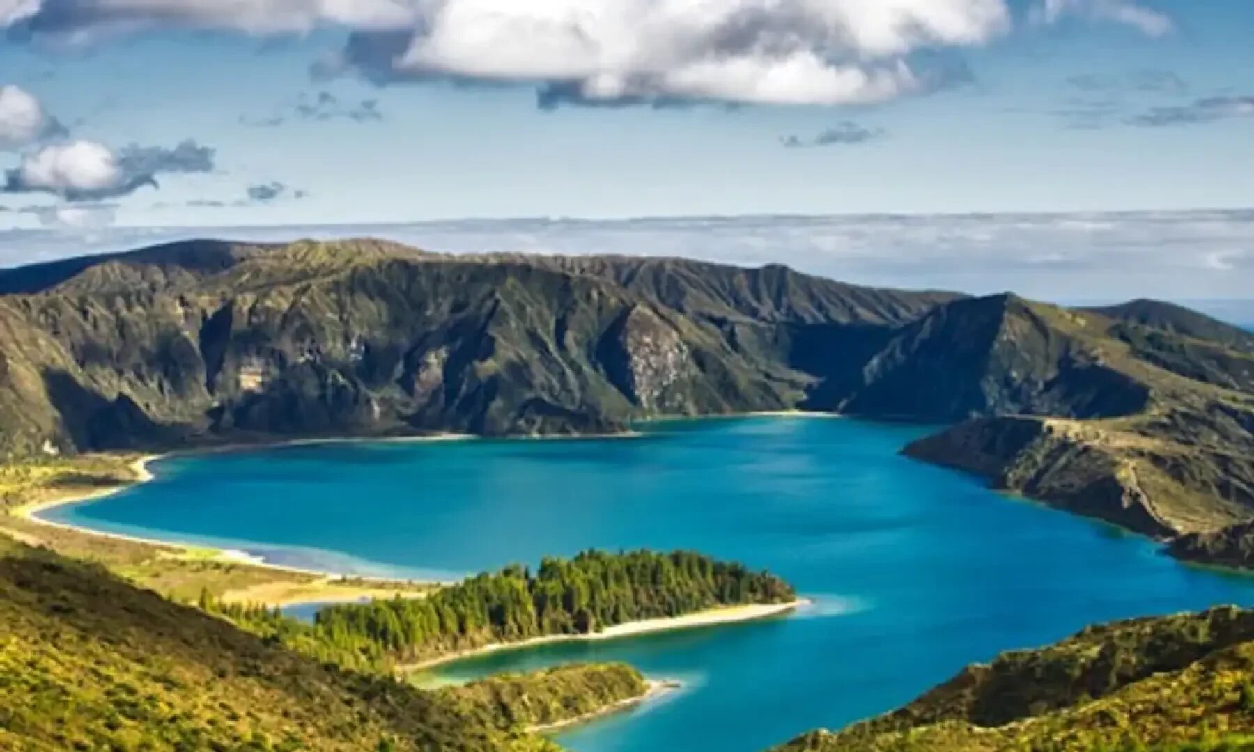 Ein leuchtend blauer See ist von grünen Hügeln und zerklüfteten Bergen unter einem teilweise bewölkten Himmel umgeben, mit üppigen Wäldern entlang des Ufers und Sonnenlicht, das die Landschaft beleuchtet.