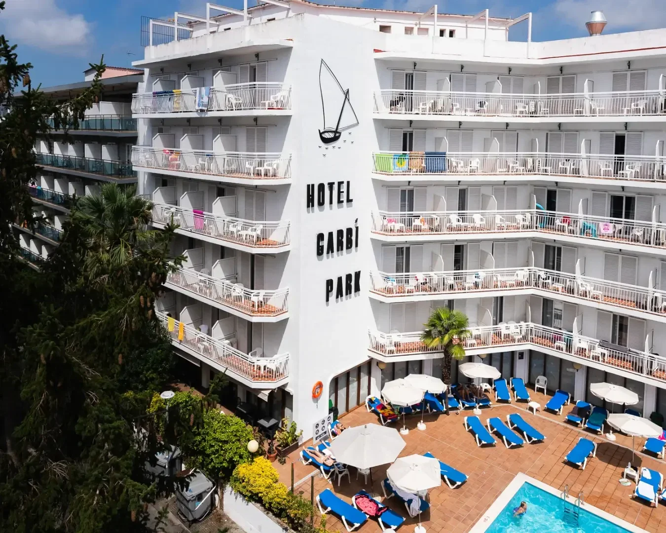 Ein weißes, mehrstöckiges Hotel mit Balkonen, das Hotel Garbí Park, überblickt einen Poolbereich mit blauen Liegestühlen, Sonnenschirmen und Gästen, die sich in der Sonne entspannen. Das Gebäude trägt das Logo eines Segelboots.